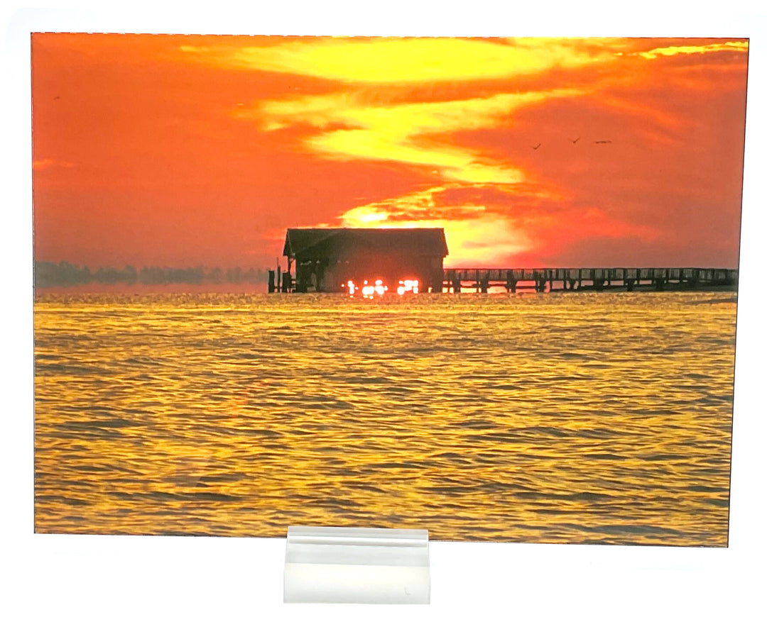 Bright sunrise over the ocean. Picture has a dock going out into the water and the sky is very yellow/pinkish-orange. Birds are flying in the sky.