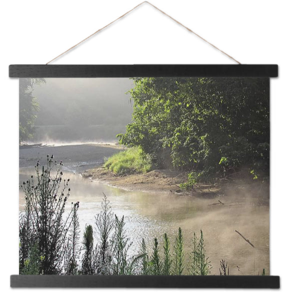 Photo is printed on hanging canvas with black border. Image is of a misty river. There is a large bushes and trees.